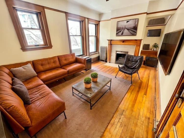 Kenosha apartments for rent - image - Chic living room featuring a luxurious brown leather sectional, sleek armchair, and a cozy fireplace with contemporary decor.