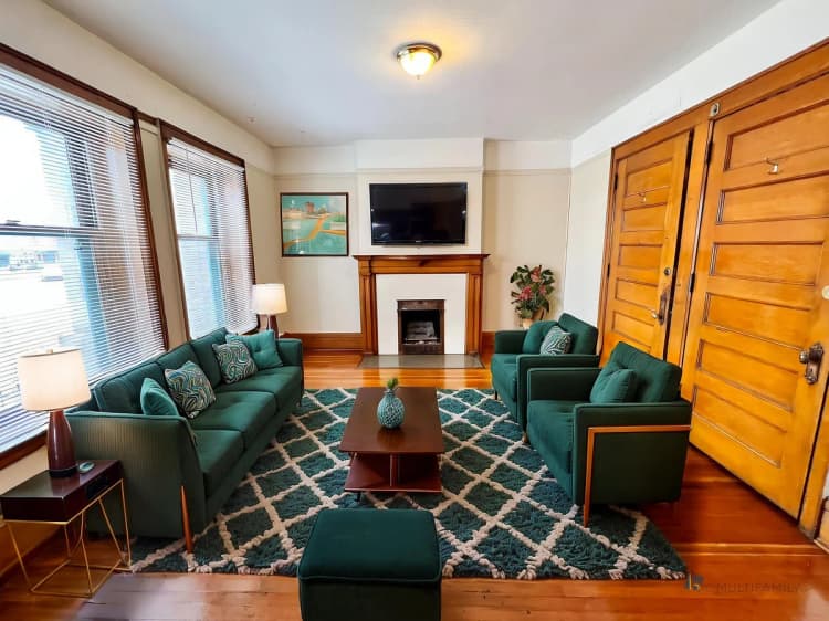 Kenosha apartments for rent - image - Inviting living room featuring elegant wood accents, plush green sofas, and a cozy fireplace, perfect for relaxation and gatherings.