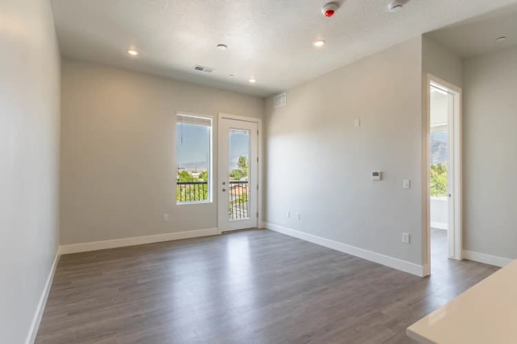 Kenosha apartments for rent - image - Bright and spacious living room featuring modern hardwood floors, large windows with scenic views, and glass door access to a private balcony.