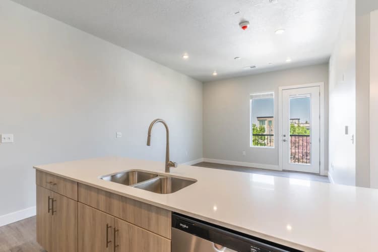 Kenosha apartments for rent - image - Modern open-plan kitchen with a sleek countertop, stainless steel sink, and bright natural light streaming through a glass door leading to a scenic outdoor view.